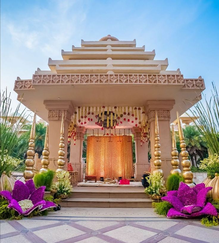 Stone temple-style outdoor mandap with carved pillars and purple floral arrangements by RAW Group
